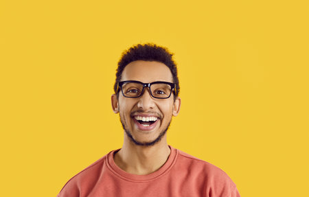 Headshot of student with happy face expression isolated on solid yellow background. Studio portrait...