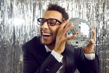 Smiling young African American showman with disco ball on party in nightclub. Happy millennial black...