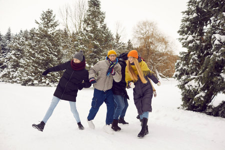Group of cheerful active millennial friends in warm clothes walking in a winter forest. Happy young...