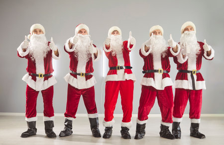 Business team of Santa group in office. Five staff in red costume give thumbs up, showing teamwork, holiday cheer and Christmas celebration in studio. Clear corporate festive teamwork concept.の写真素材