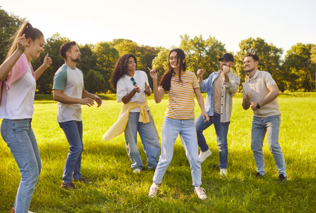 Positive friends dancing and playing together in city park, laughing during leisure party, sharing...