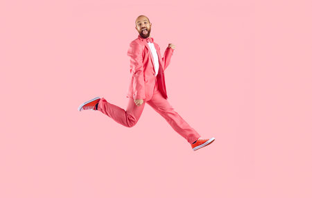 Smiling man entertainer in suit jump dance on pink studio background. Happy male performer in jacket have fun make dancing moves enjoy partying. Entertainment concept.の写真素材