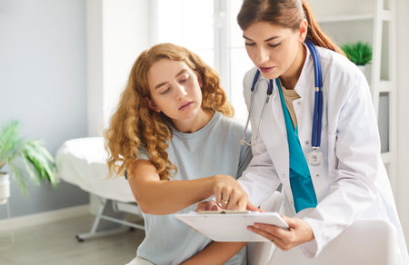 Doctor or nurse provides a medical consultation to a patient during a conversation at the hospital. The healthcare professional discusses the patient condition, focusing on checkup and examination.の写真素材