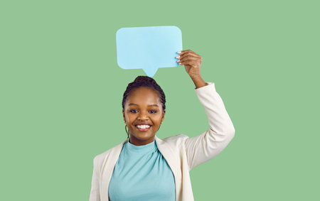 Smiling dark skinned woman holding over her head blue paper mockup speech bubble icons on light...