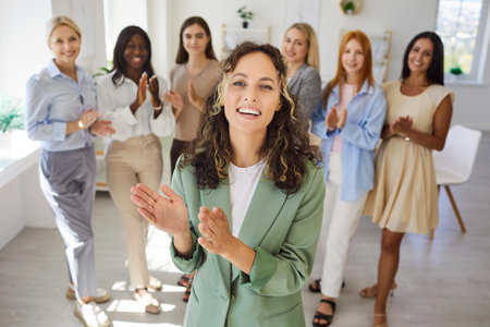 Women leadership team meeting in office. A confident portrait shows a young female leader as colleagues applaud, highlighting strategy, training, and teamwork. Core idea teamwork, business success.の写真素材