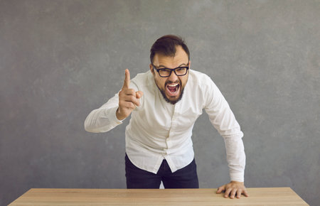 Angry man in glasses pointing finger at camera and shouting. Corporate manager arguing, quarrelling,...