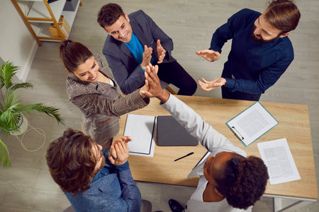 Diverse team of people meet in office and make business deal. Two happy women stand up from table...