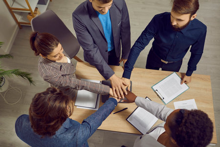 We can do anything we put our minds to. Determined to succeed, multiracial businesspeople fold their...