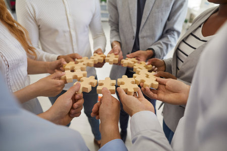 Team of business people making a jigsaw puzzle. Group of diverse men and women forming a circle with wooden jigsaw pieces they are holding in their hands. Cropped shot, close up. Teamwork conceptの写真素材