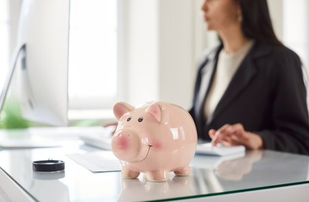 Piggy bank on office table, woman investing money, planning future, manage finances to save money, budget pay online on laptop, doing economical study on internet, making investments or strategyの写真素材