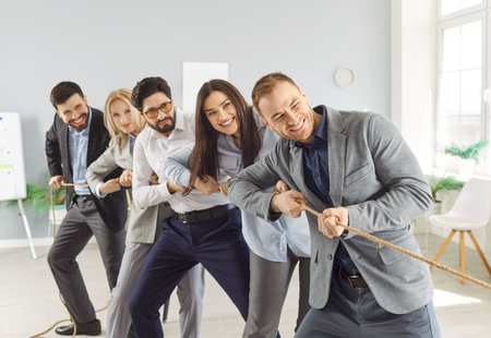 Portrait of a young cheerful business people in formal clothes pulling a rope in the office. Company...