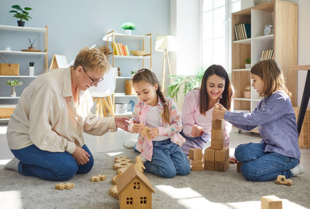 Happy young mother, senior grandmother and two children sitting on floor playing an educational game...
