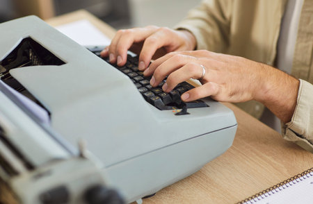 Close up of author or writer typing on vintage typewriter at desk in office shows hands over keys, paper loaded, focused on drafting and editing. Clear analog focus and productivity.の写真素材