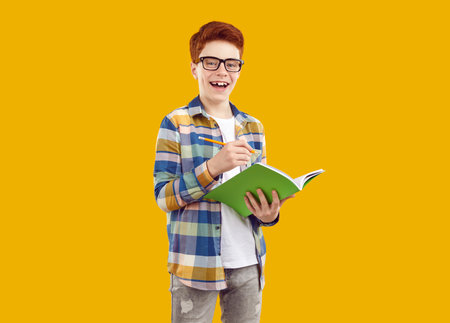 Portrait of happy school child with notebook. Happy cheerful joyful ginger student boy in casual...