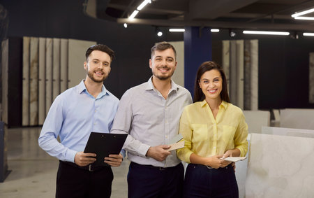 In a showroom, sales consultant meets a couple choosing interior materials. Smiling faces suggest positive dialogue, trust, and support during decision making. Depicts client service and trust.の写真素材