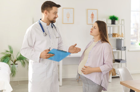 Young pregnant woman talking with her male gynecologist doctor in hospital or medical clinic. Obstetrician doctor consulting female patient expecting a baby about pregnancy during check up.の写真素材
