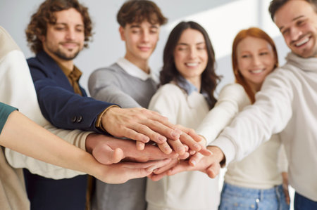 Smiling diverse group of young people standing together and stacking hands in unity and support....