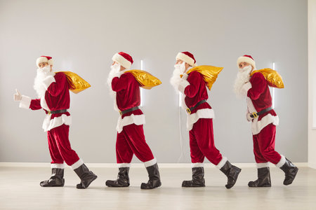 Positive Santa Claus group carries gift bags on gray background, marking christmas or new year, spreading celebration and party fun, delivering entertainment with festive holiday spirit.の写真素材
