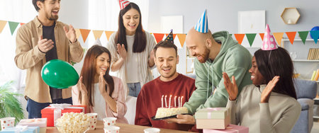 Smiling diverse people congratulating happy male friend sitting at festive table on birthday party at home. Young men and women gathering together celebrating holiday. Celebration concept. Banner.の写真素材