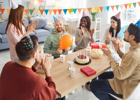 Happy diverse people group congratulating a smiling friend sitting at festive table on birthday party at home. Young men and women gathering together celebrating holiday. Celebration concept.の写真素材
