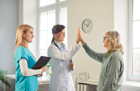 Image of female doctor giving high five to mature woman patient, reaching agreement in treatment, have checkup meeting in hospital. Sick pensioner curing in retirement house. Old people and healthの写真素材
