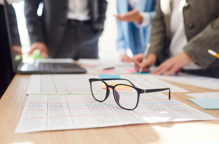 Closeup of financial documents at desk with a group of business people standing on workplace in meeting room discussing company finance growth analyzing data stat. Teamwork and cooperation concept.の写真素材