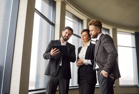 Group of three young confident business people discussing a work project during a meeting. Coworkers and employees discussing company finance and talking in modern office. Team work concept.の写真素材