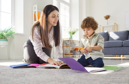 Mother and child learning and study at home. Patient parent guides a focused toddler kid with books, explaining tasks, building confidence and focus. Family, education and learning concept.の写真素材
