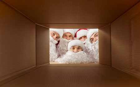 Portrait of a happy Santa team peeking into gift box, celebrating new year or christmas, sharing holiday joy, holding team spirit, enjoying festive moment with happy holiday engagement.の写真素材