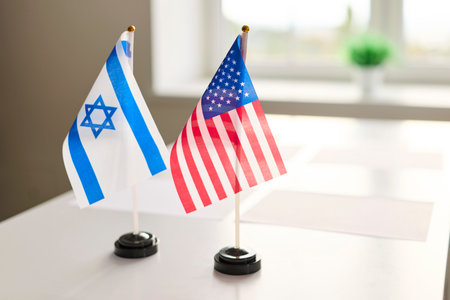 Flags signal diplomacy, meeting and negotiation at table. Israel and USA flags signal bilateral discussion and international agreement. Symbolic concept: diplomatic cooperation and partnership.の写真素材