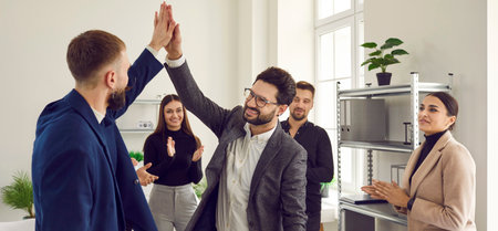 Two business men giving high fiving each other in office. Business colleagues applauding them celebrating success and supporting. Shot of business people during informal meetingの写真素材