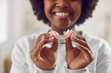 Happy, smiling young African American woman holding a teeth whitening tray. Close up of hands...
