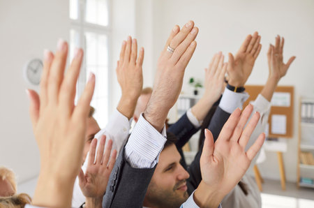 Close up cropped shot of hands raised by business professionals in formal attire during meeting in...
