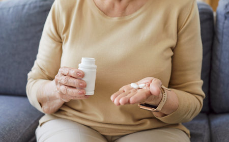 Closeup cropped photo of senior woman hands holding jar of pills going to take medical preparations sitting on couch at home. Retired female person taking painkillers using medications.の写真素材