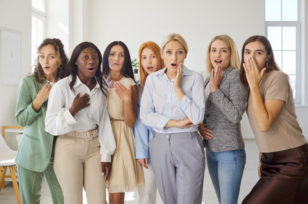 Women group share surprise, shock, and emotion. Female team stand in office, eyes wide, mouths open, showing amazed reaction with friends and teamwork. Concept collective surprise and unity.の写真素材