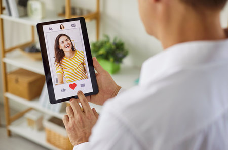 Closeup of a person using a smartphone dating app, tapping the heart icon to like a users profile in a living room, showing screen and finger interaction. Find love and online dating concept.の写真素材