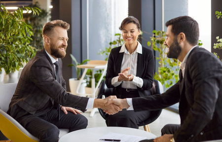 Group of successful company employees making deal sitting in modern office. Happy smiling business people in formal clothes shaking hands on meeting. Teamwork and partnership concept.の写真素材