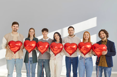 Team of young people holding heart shaped balloons. Group of happy smiling casual corporate employees friends with red balloons in hands standing in office. Valentines day, love, friendship conceptの写真素材