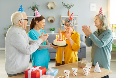 Happy birthday, senior people candles blowing cake, celebration for friendly group of old elderly with nurse, caregiver, carer, support worker, active seniors in social recreational friendship clubの写真素材