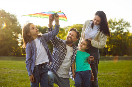 Portrait of happy cheerful family playing with flying kite walking in park on weekend. Father, mother and two children boy and girl enjoying summer together outdoors. Family leisure concept.の写真素材