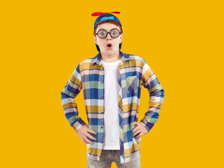 Funny preteen boy looking at you with omg facial expression on orange background in studio. Portrait of amazed Caucasian teenage boy in humorous glasses with magnifying lenses and in childs cap.の写真素材