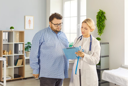 Patient and doctor consultation in medical clinic. Overweight fat man listens as female physician reviews notes, discusses obesity risks and treatment. Healthcare guidance and support concept.の写真素材