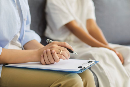 Psychologist counseling child during support session. Close-up of therapist hands clipboard in office, patient sits, showing healthcare and psychology. Professional family care, child therapy.の写真素材