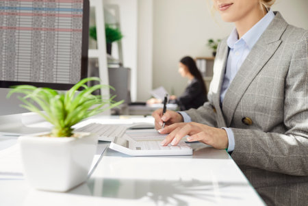 Cropped shot of woman business accountant in formal suit working in office with database, making analysis and calculation, sitting at white table, entering data in electronic files.の写真素材