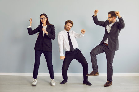 Three young business people and company employees in suits dancing having fun and celebrate their...