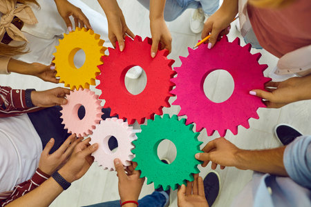 Team of people, students or corporate workers, standing in circle, holding colorful cogs and joining them. Cropped shot of hands with gears. Teamwork, business, education, success concept backgroundの写真素材