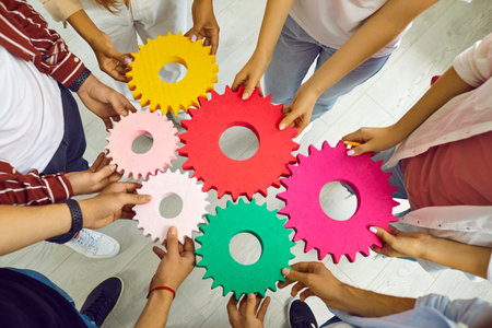Team of people connecting gears. Cropped shot group of young men and women standing in circle and joining colorful cogs together. Teamwork, integration, business, education, success concept backgroundの写真素材