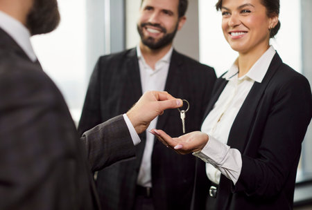 Close up view of smiling businesswoman receiving key from partner after successful deal. Happy businessman watching agreement completion, symbolizing real estate, investment or ownership transfer.の写真素材