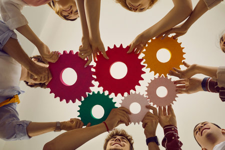 Colorful gears in hands of positive college students standing in circle and connecting them. Young people are looking for ways to solve problem by studying educational training courses. Bottom view.の写真素材