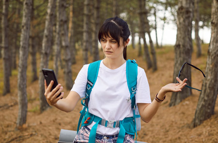 Lost hiker in forest with smartphone. Tourist woman check map app and GPS signal, frustrated by no connection backpack on, frustration about navigation and safety. No signal, offline maps and hiking.の写真素材